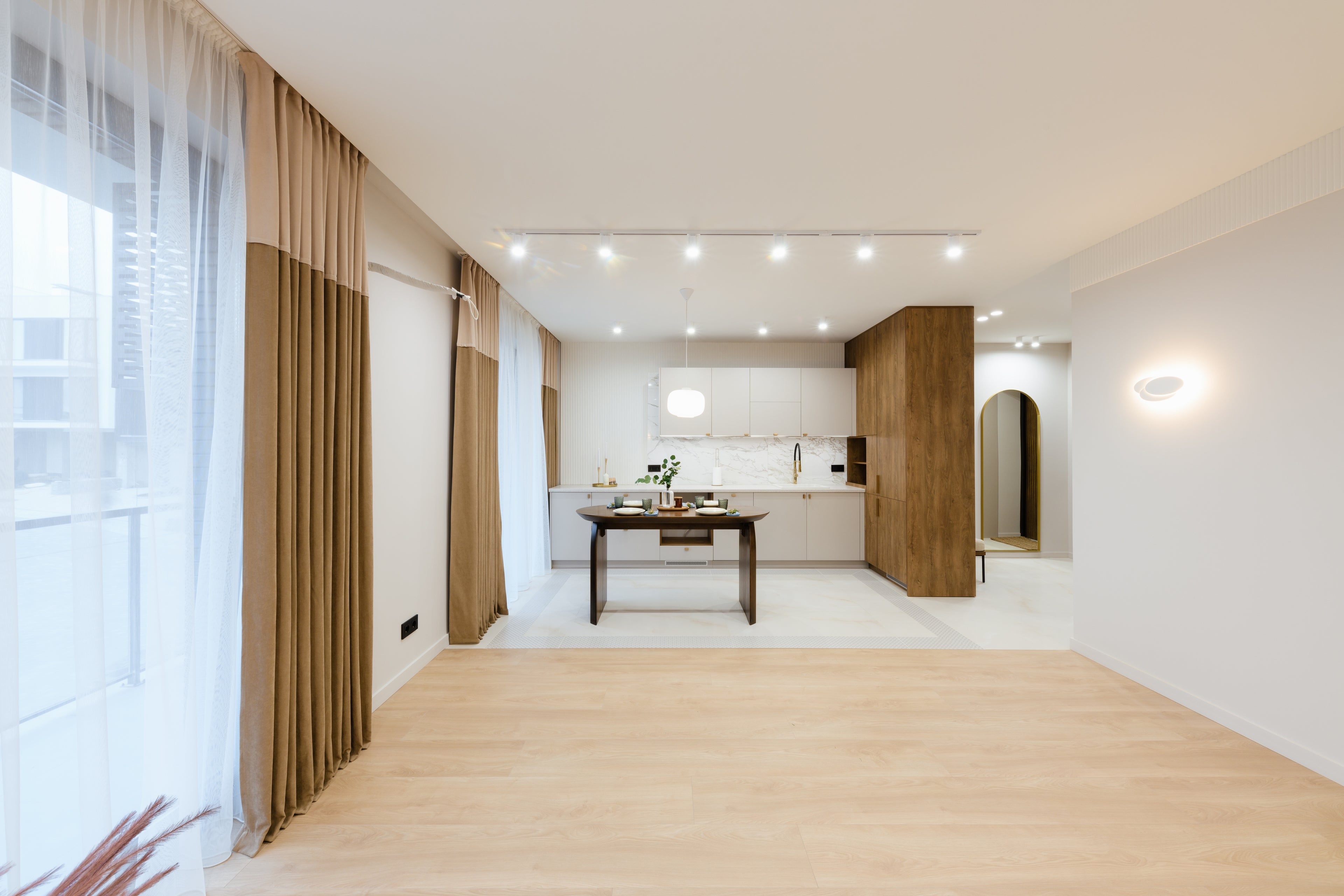 Modern interieur met open keuken, houten vloer, beige gordijnen en warme verlichting. Strakke kasten en een eettafel creëren een sfeervolle ruimte.