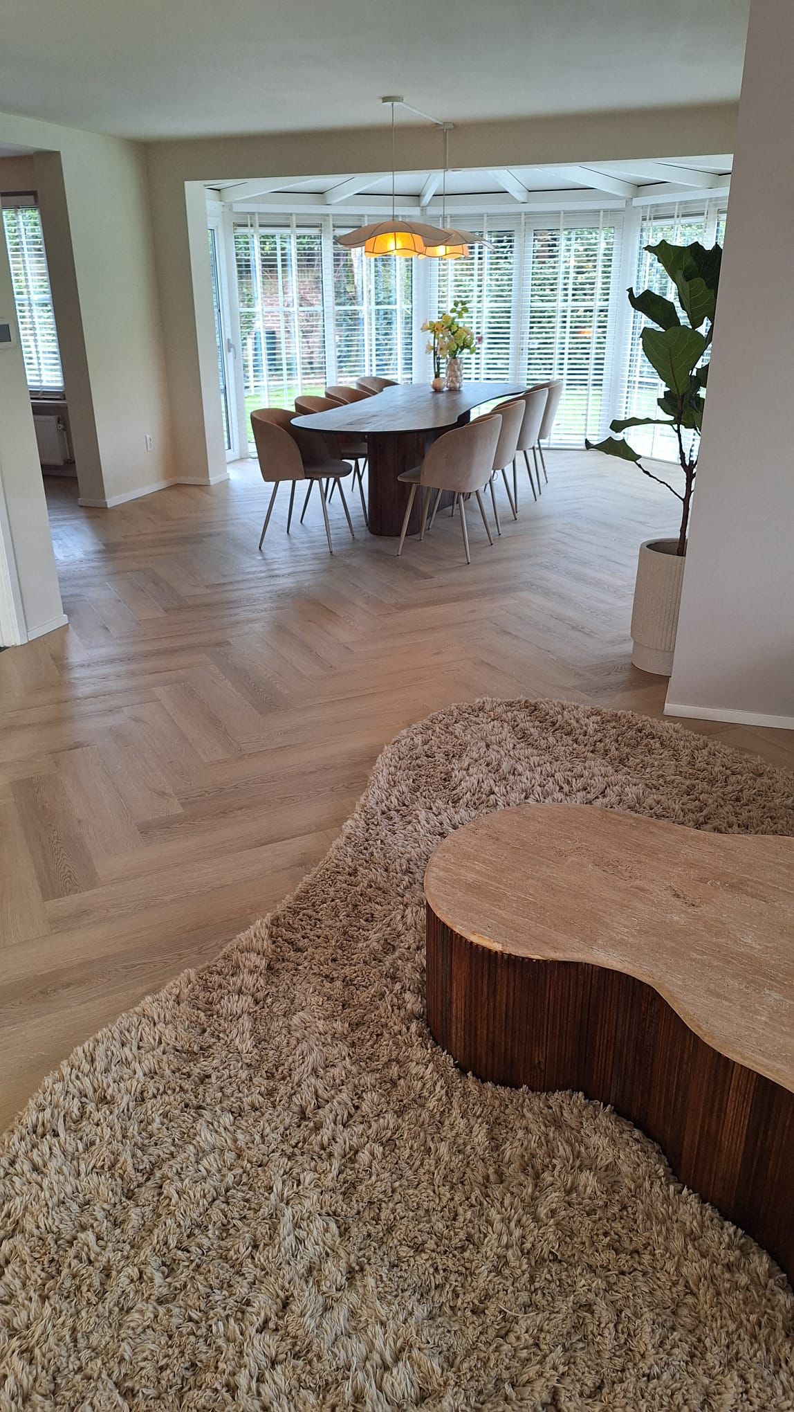Lichte houten visgraatvloer met een natuurlijke uitstraling, gecombineerd met een hoogpolig beige vloerkleed voor contrast en warmte.